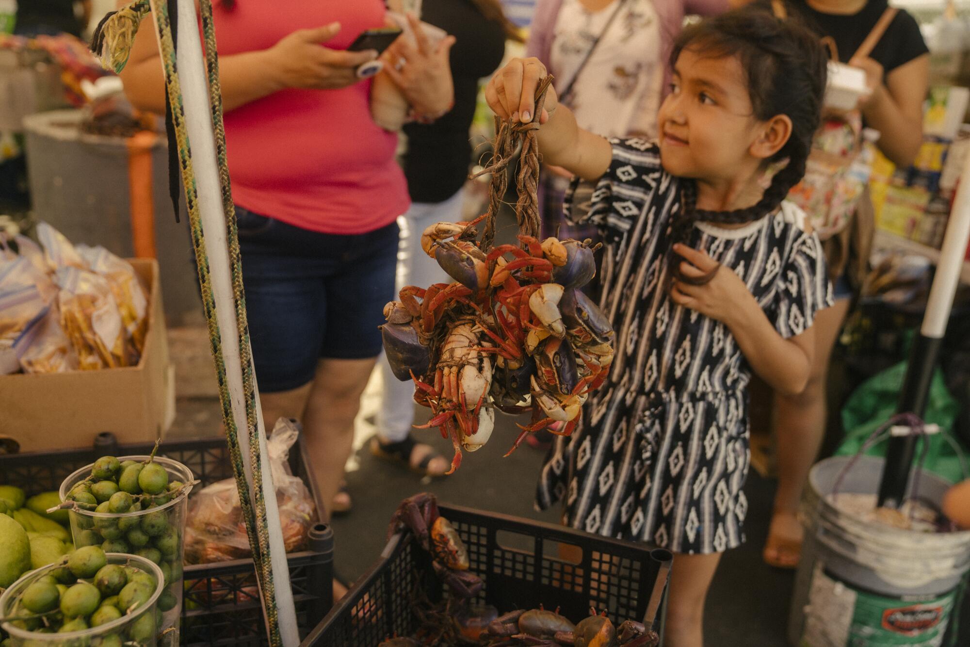 A girl holds up crabs for sale at the Salvadoran street food market in the parking lot of Two Guys Plaza.