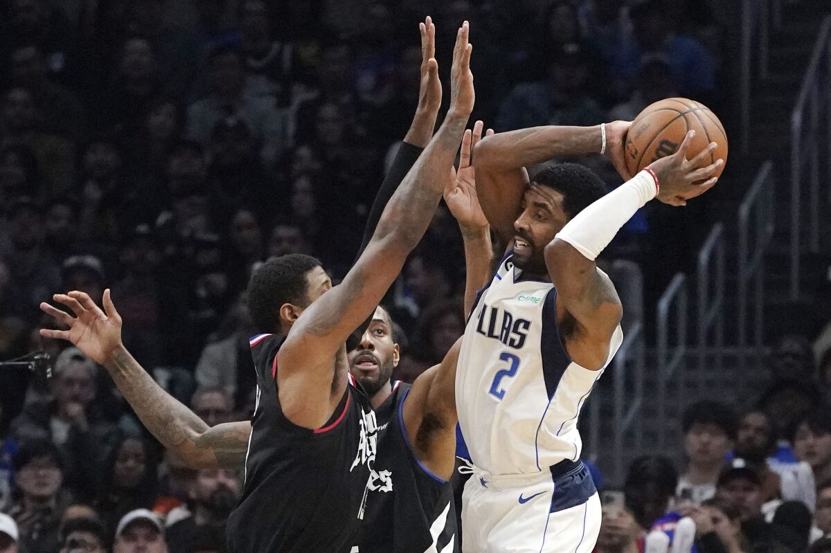 Dallas Mavericks guard Kyrie Irving, right, tries to pass while under pressure from Los Angeles Clippers forward Paul George, left, and forward Kawhi Leonard during the second half of an NBA basketball game Wednesday, Feb. 8, 2023, in Los Angeles. (AP Photo/Mark J. Terrill)
