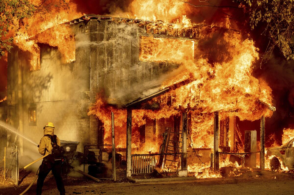 Un bombero rocía agua en un intento por impedir que un incendio se propague a residencias, en Doyle, California