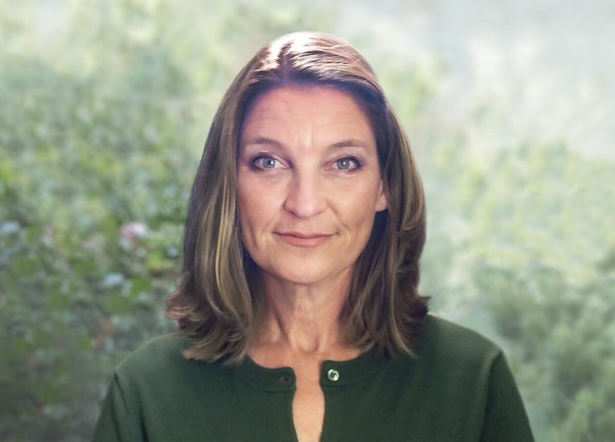 A woman in a green shirt with shoulder-length brown hair, smiling outdoors