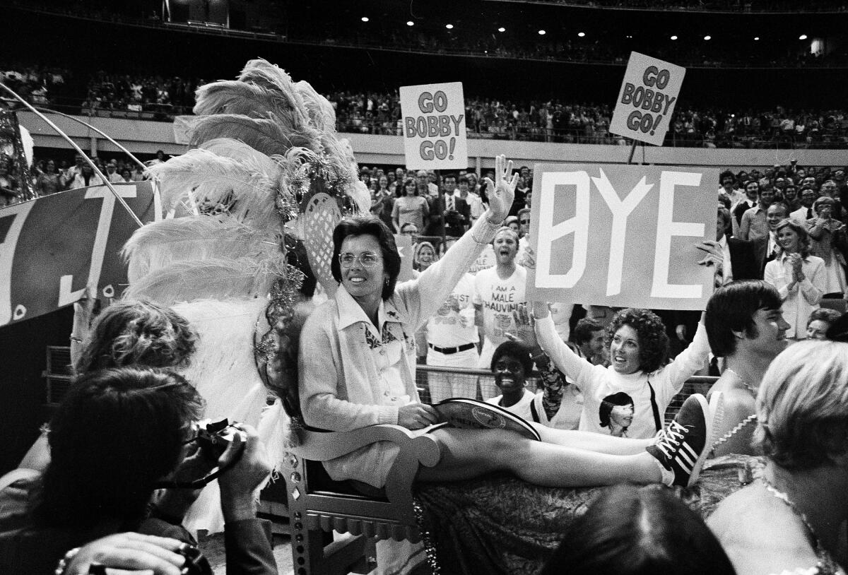 Billie Jean King is carried on a litter into the Battle of the Sexes, with "Go Bobby Go!" signs behind her.
