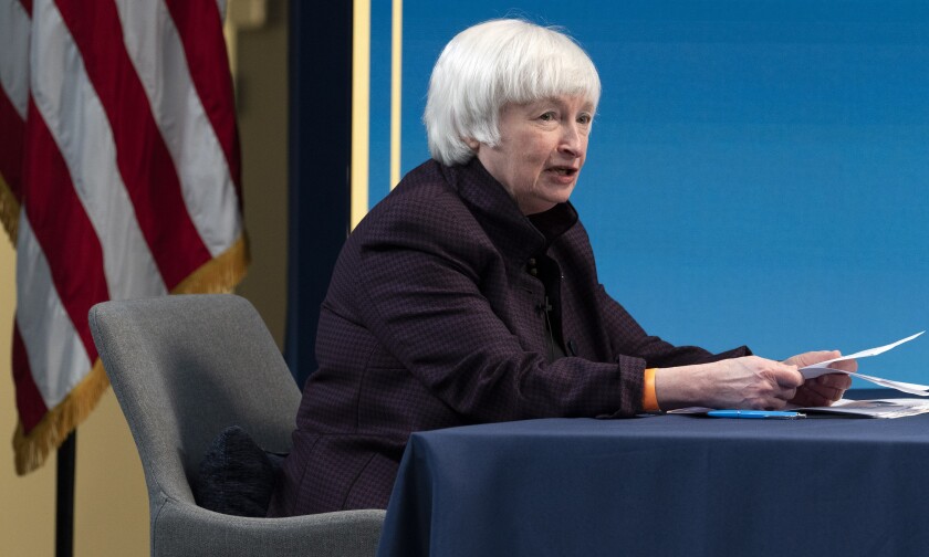 Janet Yellen speaks while sitting at a table, papers in hand.