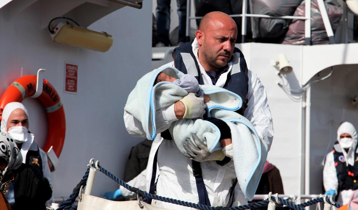 An officer carries a baby as rescued migrants disembark from an Italian coast guard vessel in the Sicilian town of Porto Empedocle on March 4.