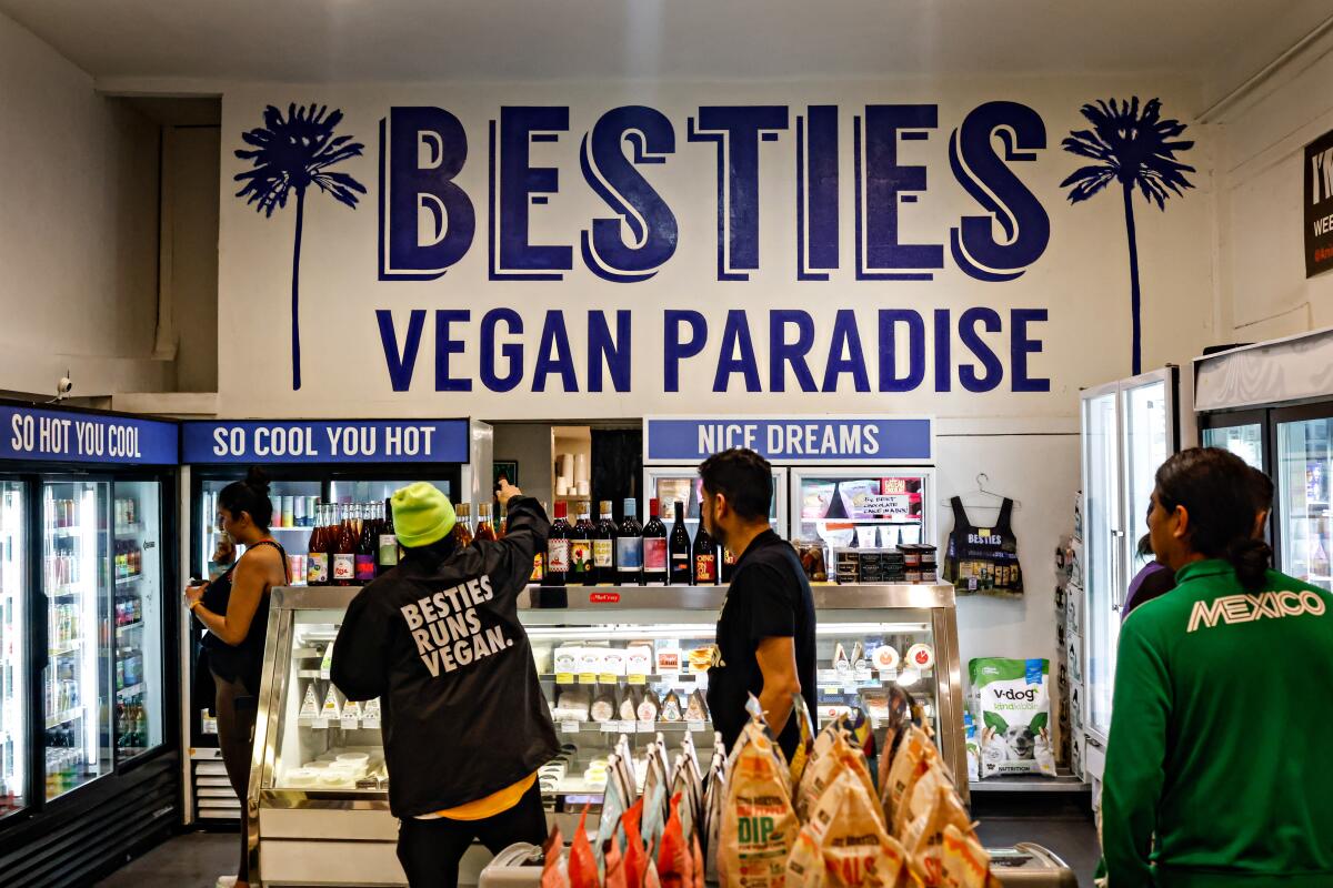 People stand at a counter in a store with the words Besties Vegan Paradise on the wall above them