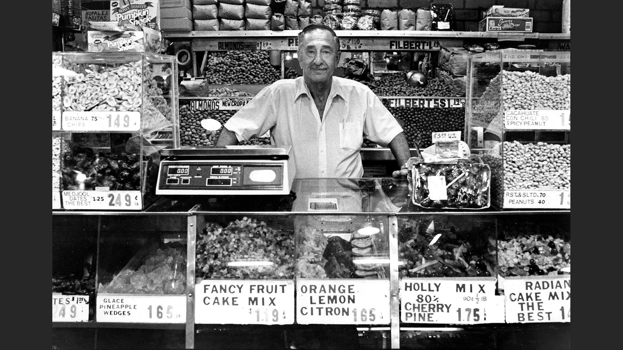 Irv Karan stands behind a shop counter, surrounded by bins of dried fruit and nuts.