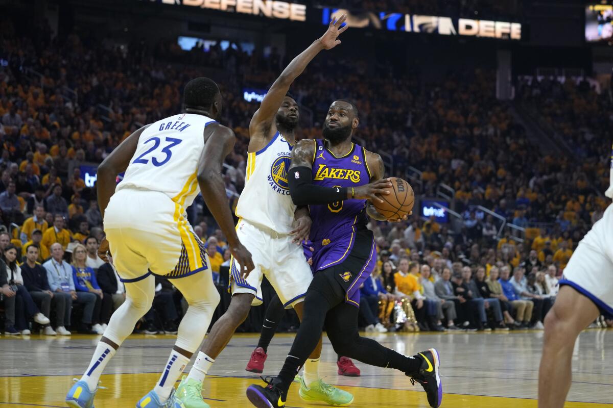 Lakers forward LeBron James, right, drives down the lane against Warriors forwards Andrew Wiggins, center, and Draymond Green