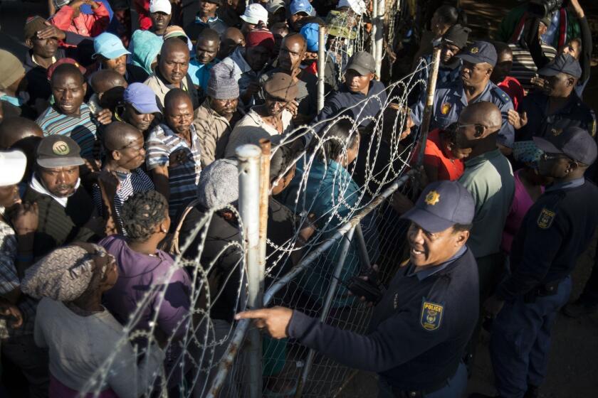 South African police guard a gate as striking platinum miners and their relatives line up to get food parcels from the South African food bank on June 13.