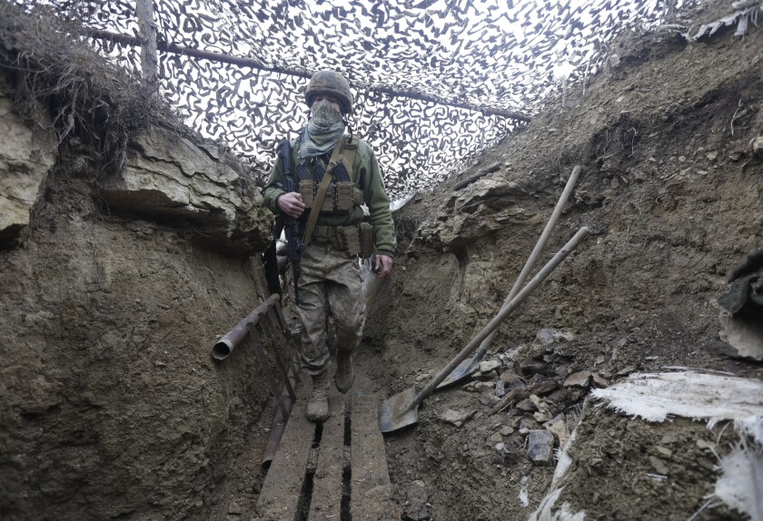 A Ukrainian solder walks in a trench under a camouflage net.
