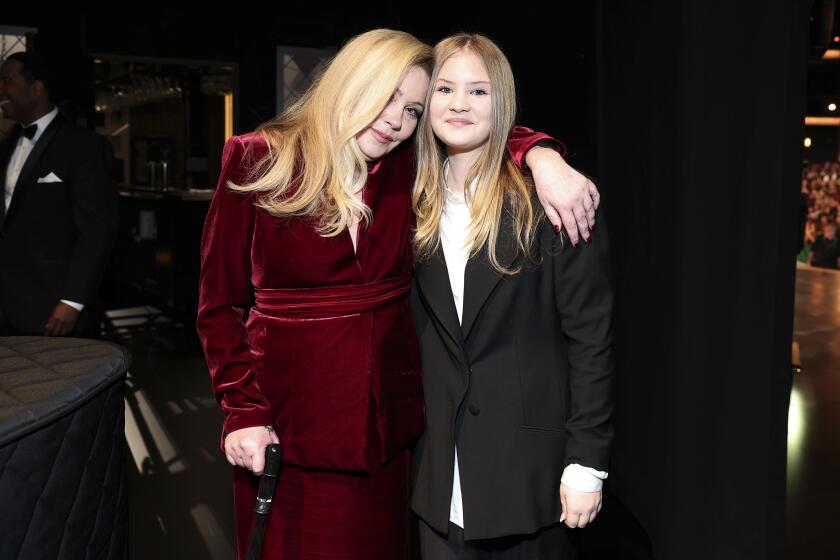 Christina Applegate in a burgundy velvet gown leaning her head on her daughter's shoulder. Her daughter wears a black suit