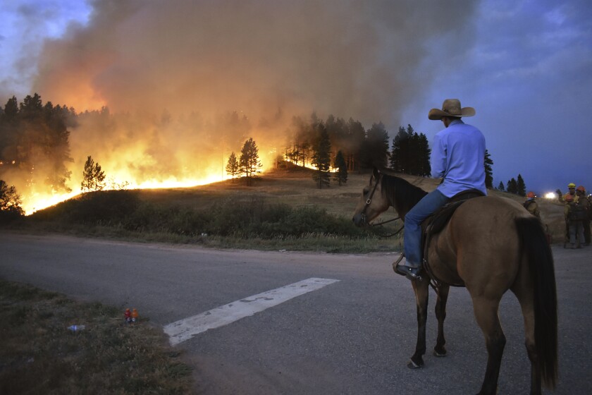 A man on horseback watches a wildfire across a road
