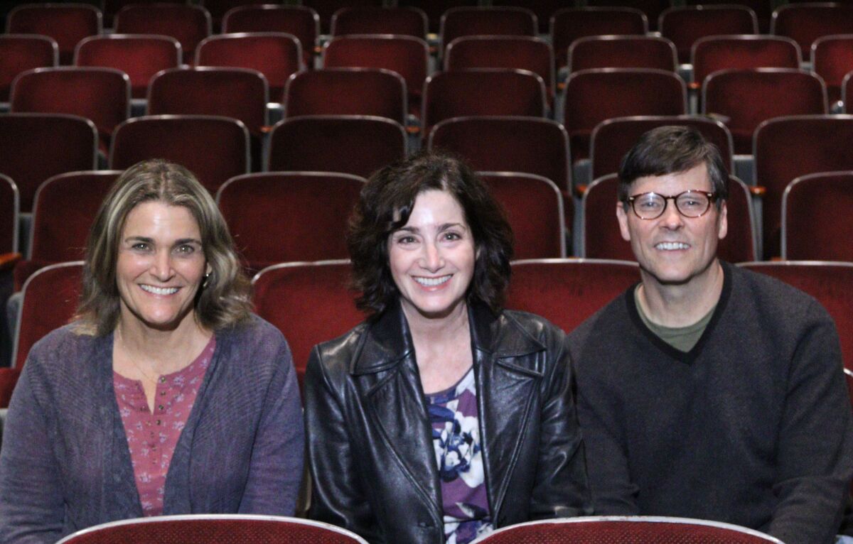 Two women and one man sit inside a theater auditorium.