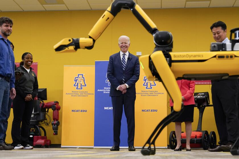 President Joe Biden looks at Spot, a Boston Dynamics robotic dog, during a tour with professor Sun Yi, right, of the Department of Mechanical Engineering, North Carolina Agricultural and Technical State University, at North Carolina Agricultural and Technical State University, in Greensboro, N.C., Thursday, April 14, 2022. (AP Photo/Carolyn Kaster)