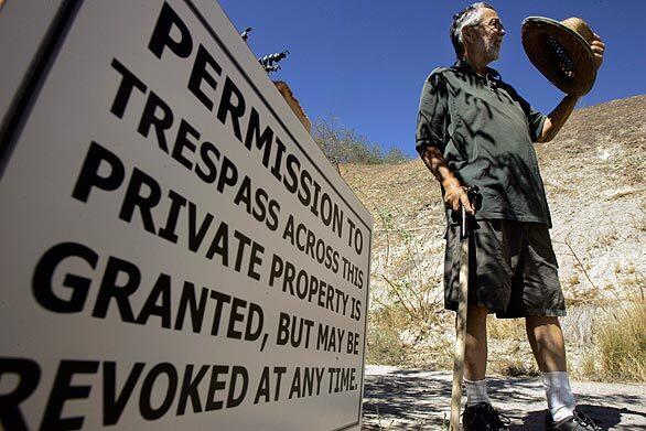 Gardner Compton stands next to the sign in front of the gate he erected to block access to homes on Forest Park Drive. Compton says he will extend the blockade to pedestrian traffic this weekend.