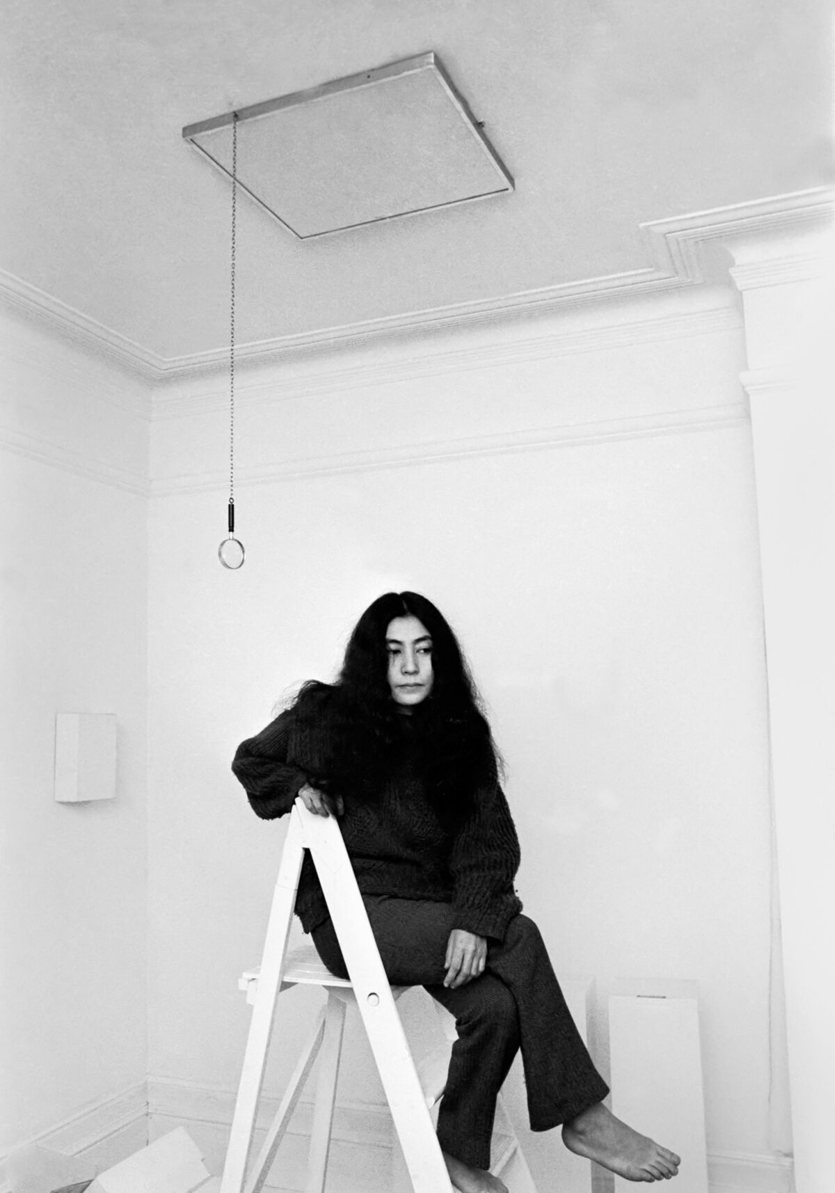 A black-and-white photograph of a woman with long hair sitting on a ladder.