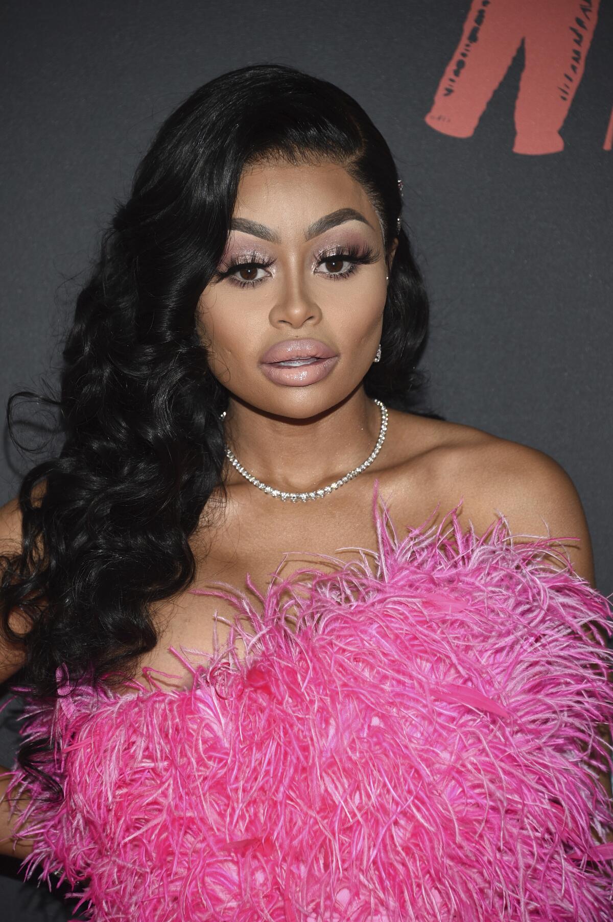 A woman with dark hair wears a diamond necklace and a pink strapless feathered dress.