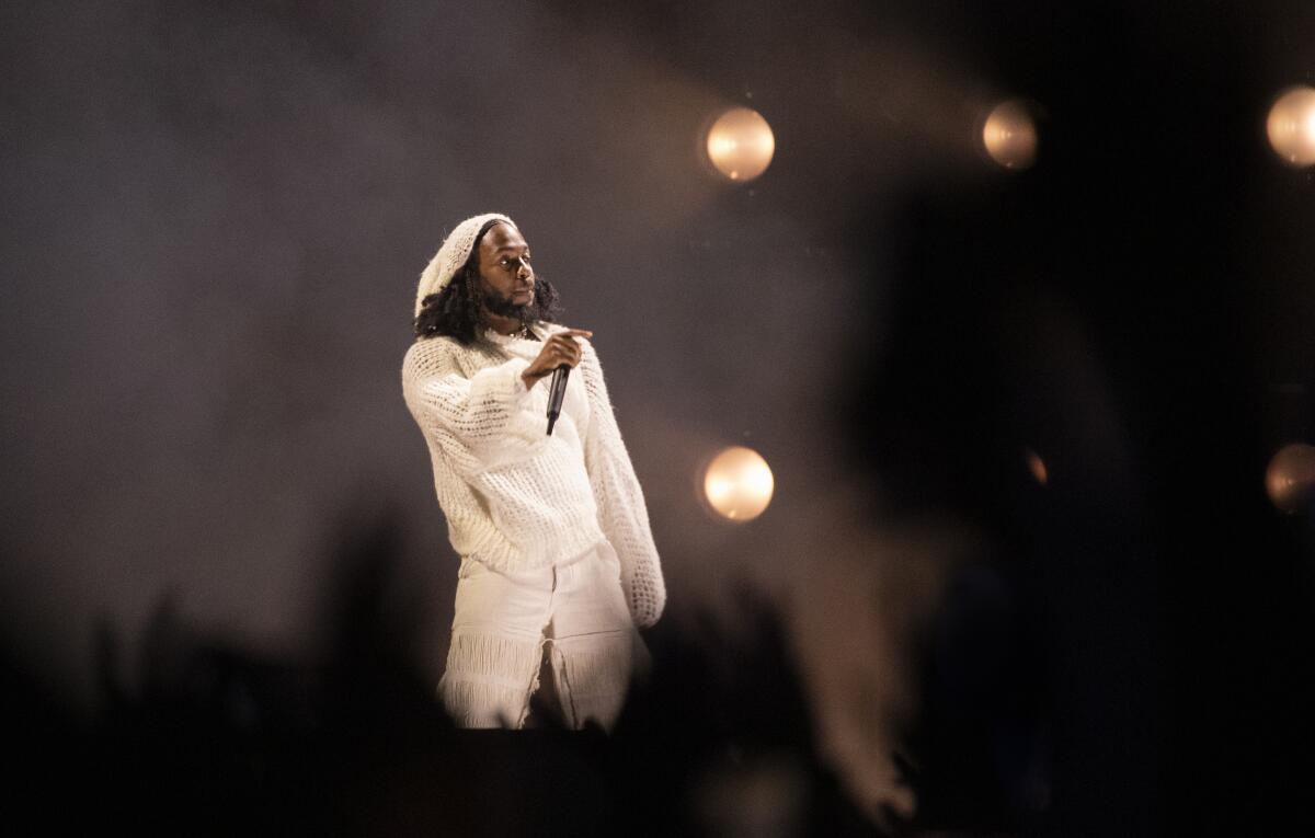 A man in a white knit hat, sweater and pants performs onstage