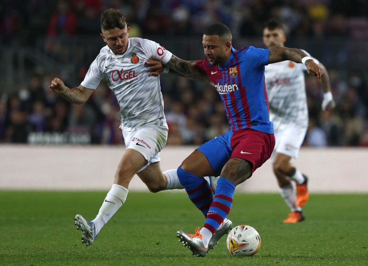 Barcelona's Memphis Depay, right, challenges for the ball with Mallorca's Pablo Maffeo during a Spanish La Liga soccer match between FC Barcelona and Mallorca at the Camp Nou stadium in Barcelona, Spain, Sunday, May 1, 2022. (AP Photo/Joan Monfort)