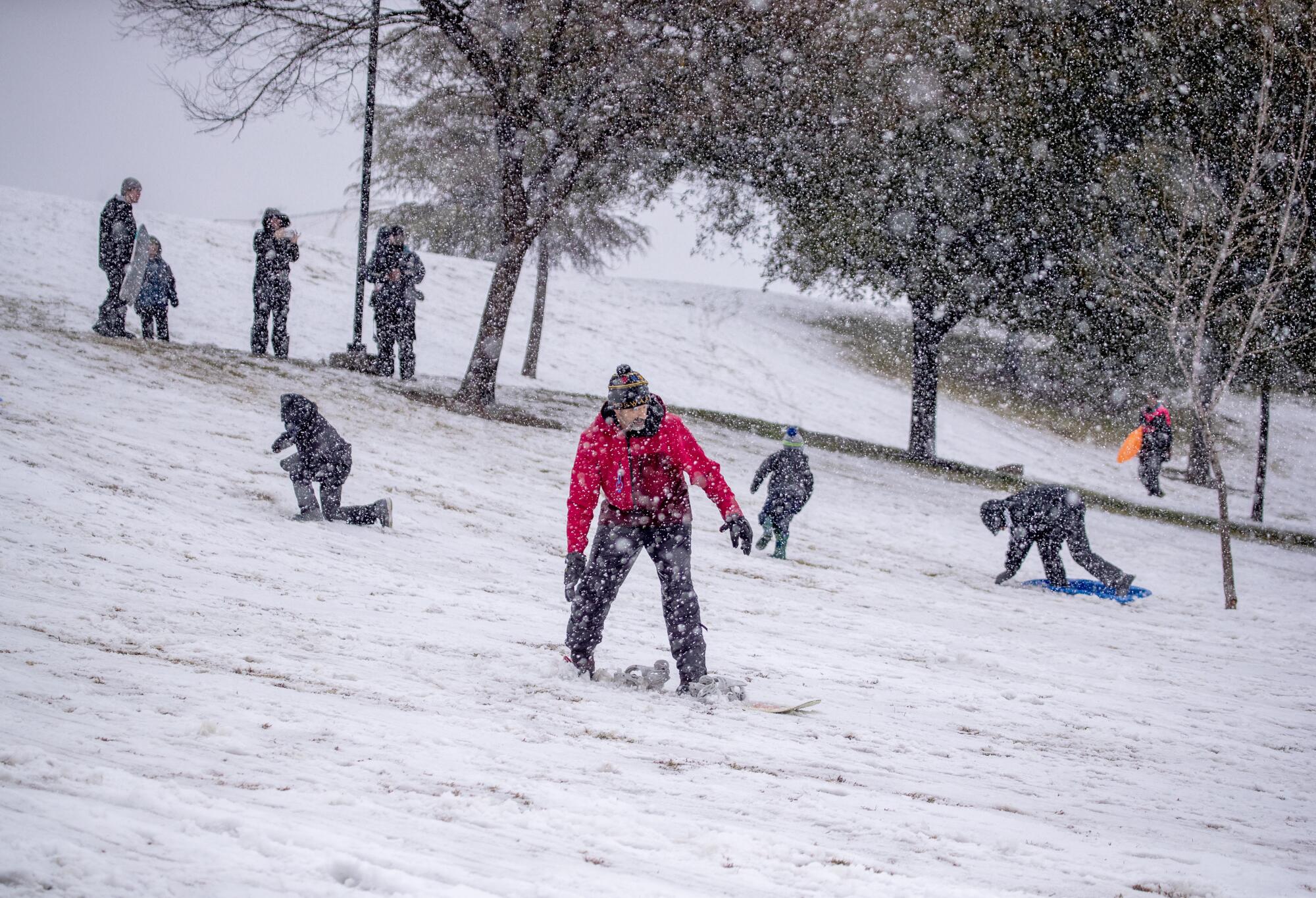 People snowboard and sled down a hill as snow still falls.