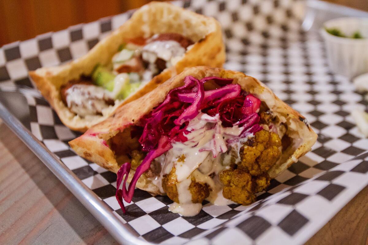 Two halves of pita bursting with cauliflower shawarma, front, and tricolor falafel from B'ivrit in Cypress Park.