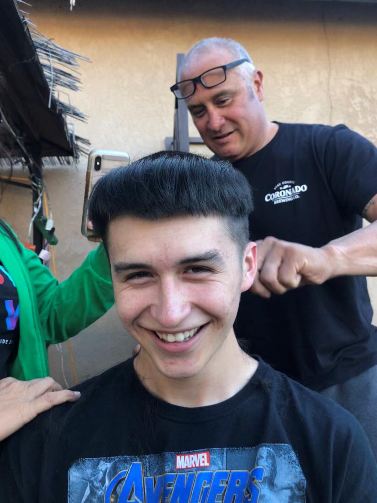 Steven Alvarez, 19, laughs as his dad, Steve Alvarez, gives him a monk hairstyle during a home hair-cutting livestream March 23 in the family's Chula Vista backyard.