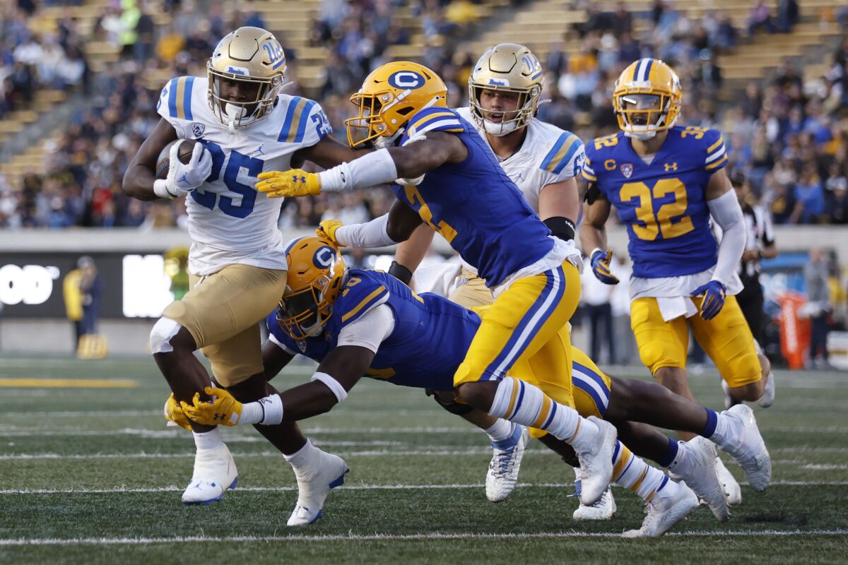 UCLA running back TJ Harden tries to evade California safety Craig Woodson (2) and another defender.