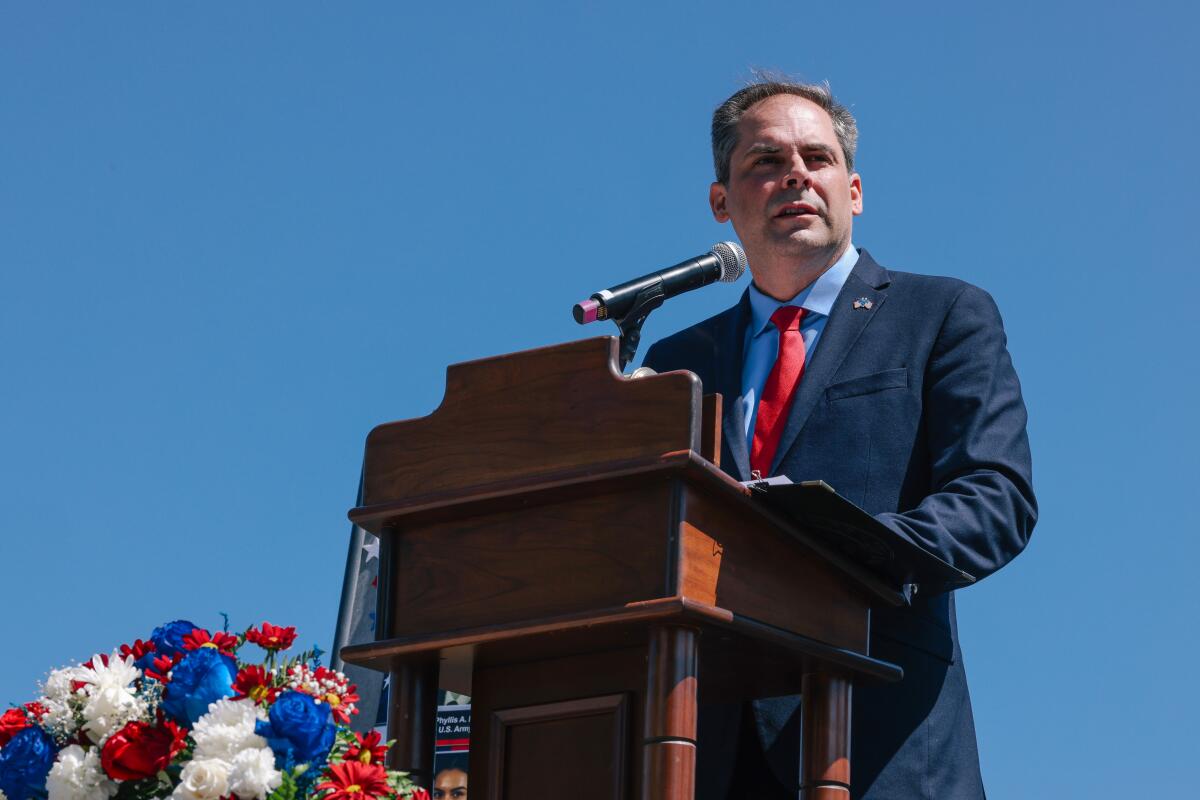 A man in a blue suit and red tie speaks from a lectern.