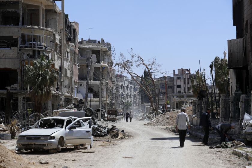 FILE - Syrians walk through destruction in the town of Douma, the site of a suspected chemical weapons attack, near Damascus, Syria, Monday, April 16, 2018. A report published Friday, Jan. 27, 2023, by a team from the Organization for the Prohibition of Chemical Weapons established there are “reasonable grounds to believe” Syria's air force dropped two cylinders containing chlorine gas on the city of Douma in April 2018, killing 43 people. (AP Photo/Hassan Ammar, File)