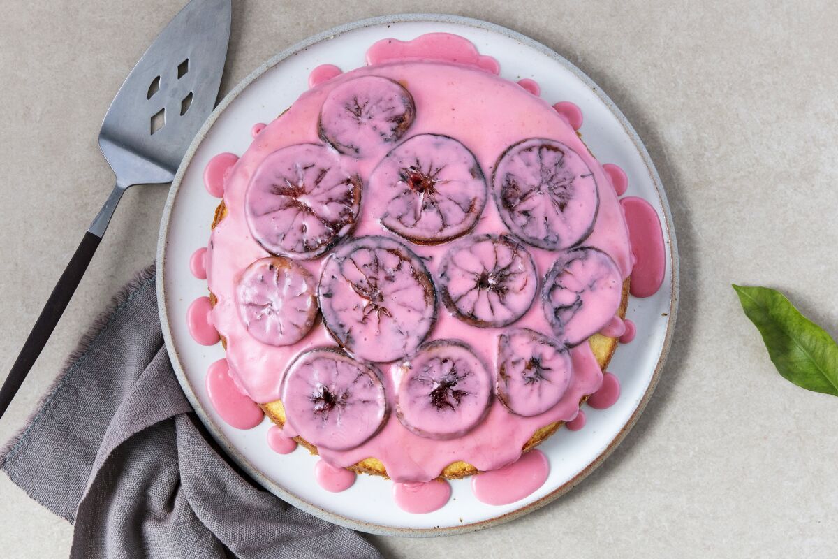 A round cake, seen from above, with a pink glaze and citrus slices on it