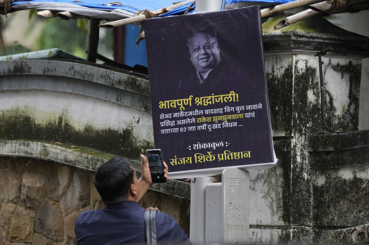A man takes picture of a poster paying homage to veteran stock market investor and Indian billionaire Rakesh Jhunjhunwala displayed outside his residence, in Mumbai, India, Sunday, Aug.14, 2022. Jhunjhunwala, nicknamed India’s own Warren Buffett, died Sunday in Mumbai city, Press Trust of India news agency reported. He was 62. (AP Photo/Rafiq Maqbool)