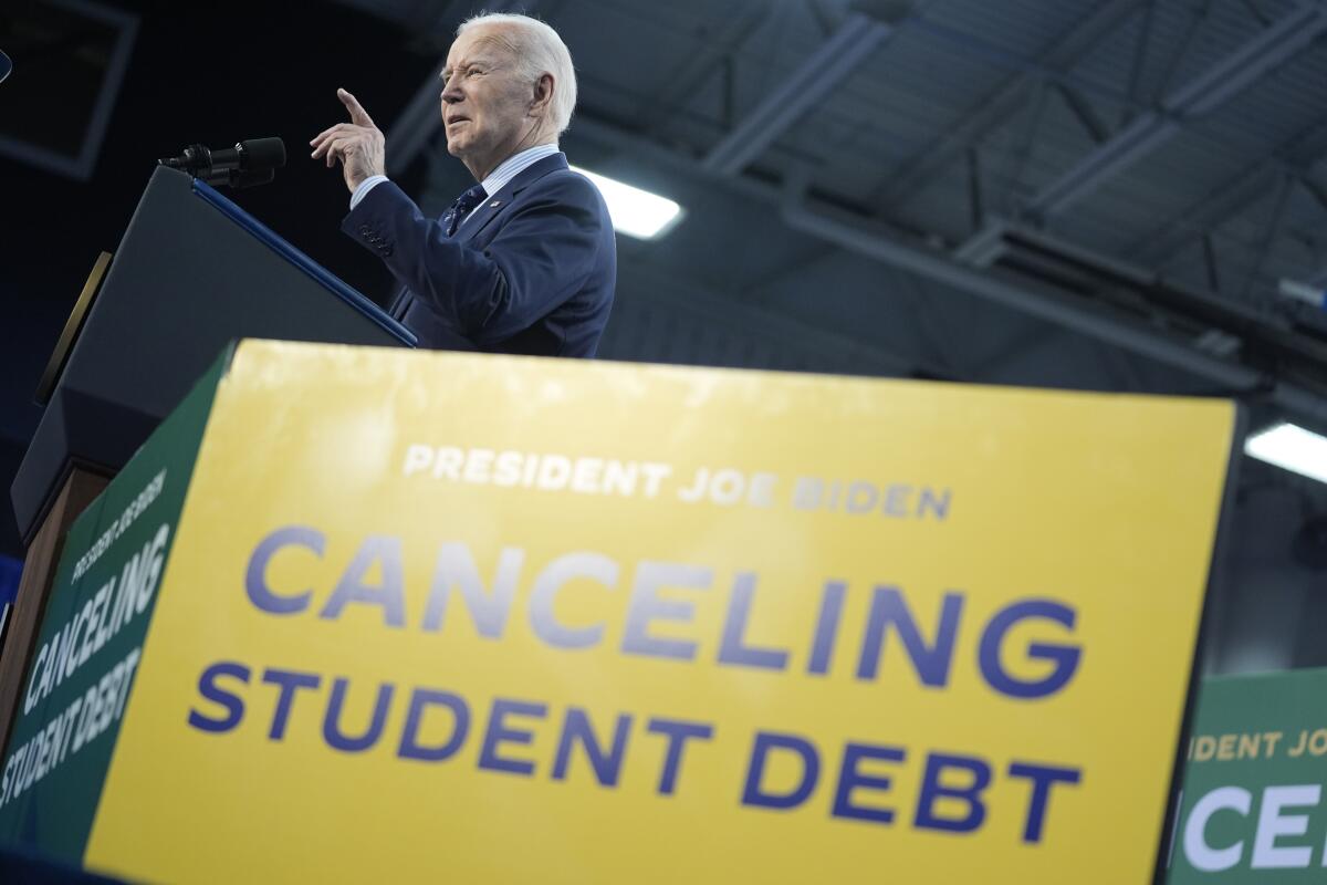 President Joe Biden delivers remarks near a sign that says President Joe Biden canceling student debt