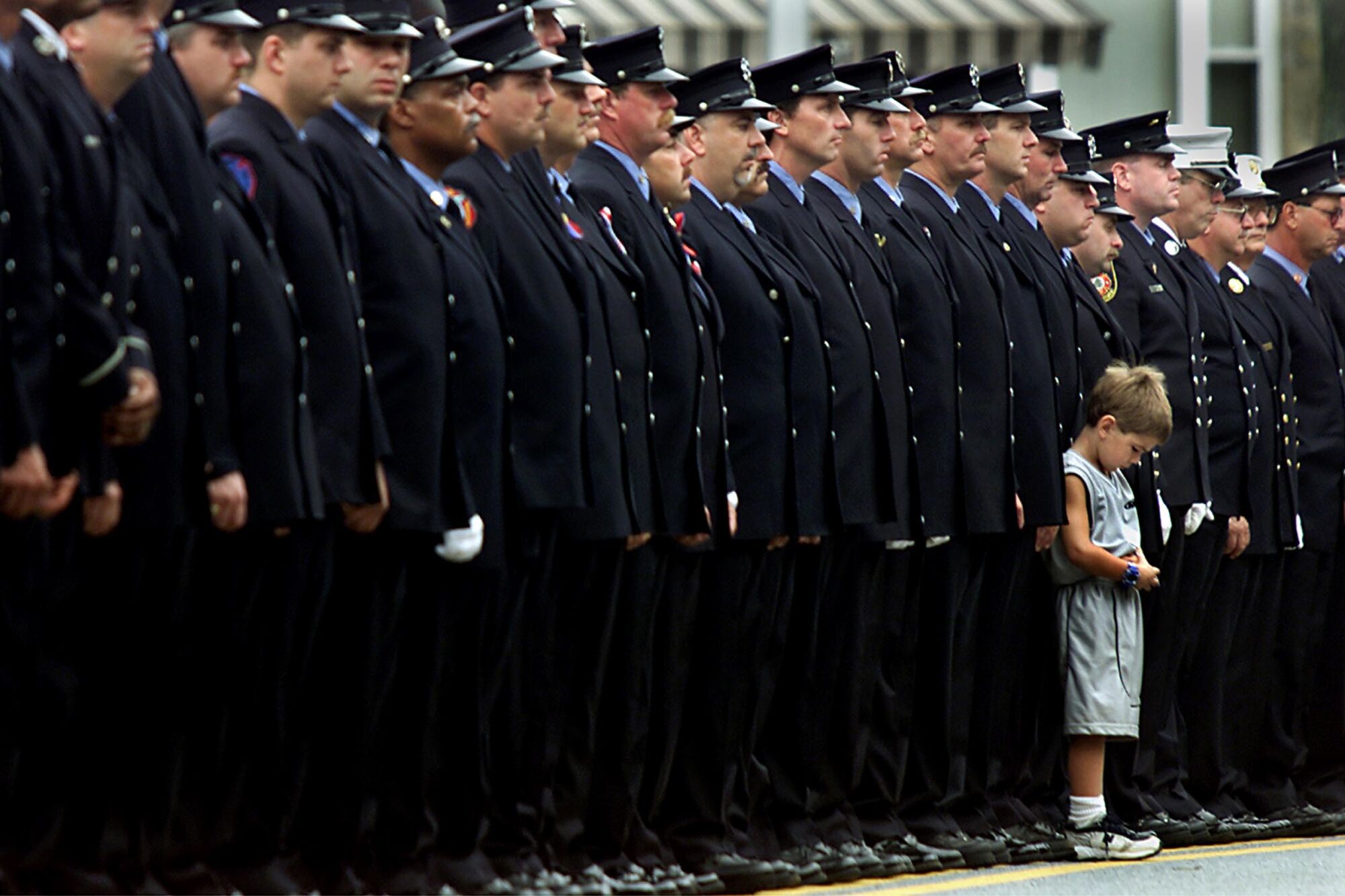 A small boy stands before a long line of firefighters