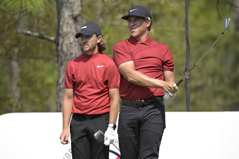 Tommy Fleetwood and Cameron Champ watch Champ's tee shot while wearing red shirts and black pants and hats