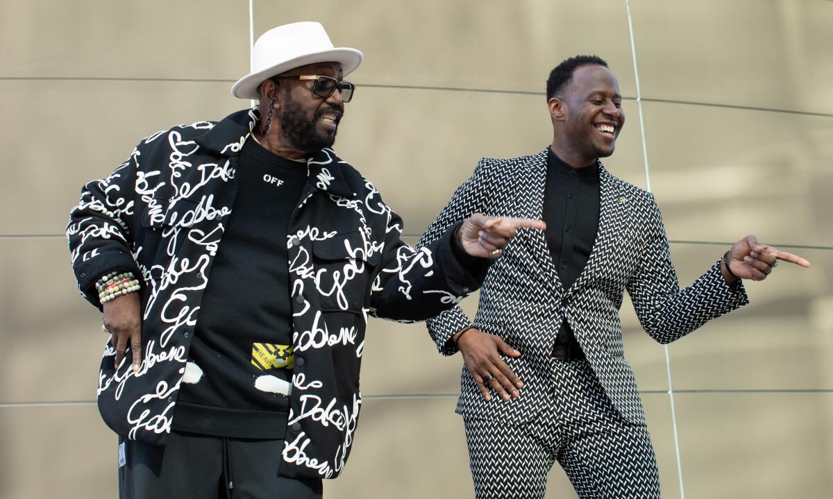 Otis Williams, in a black sweatshirt and white hat, and Marcus Paul James, in a patterned suit, do some dance moves