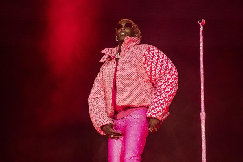 A man in a pink puff jacket and hot pink pants raps on a stage