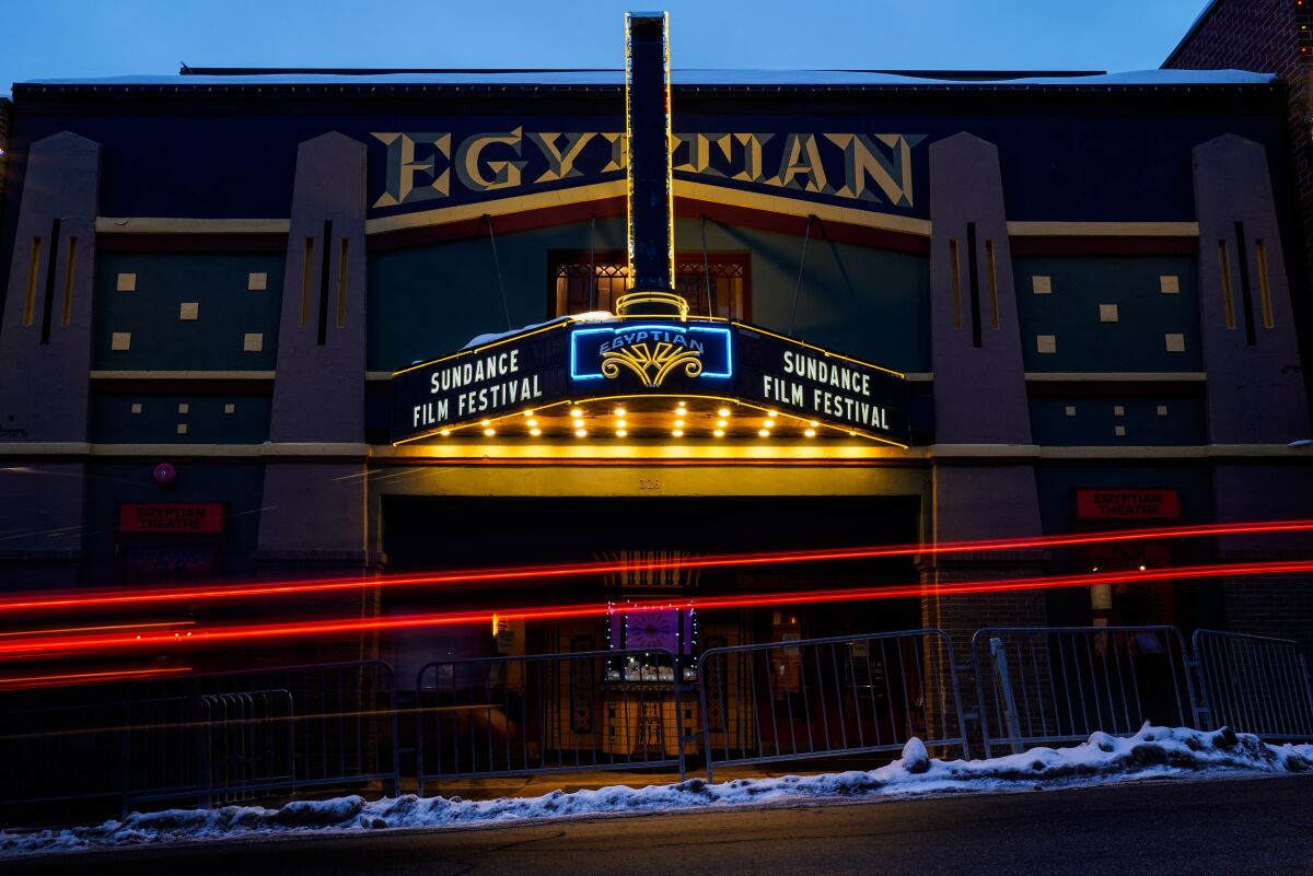Snow lines a curb and red beams indicate a passing car at the Egyptian. The marquee reads "Sundance Film Festival."