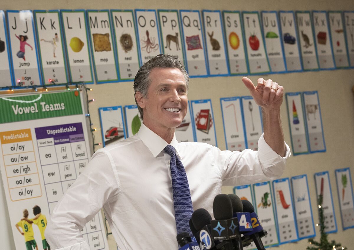 A man gesturing in front of microphones in an elementary school classroom 