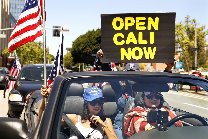LOS ANGELES-CA-APRIL 22, 2020: A group of protesters including Alma Villanueva, left, and Gigi Wilcox, right, stage a vehicle caravan protest to call on state and local officials to re-open the economy in downtown Los Angeles on Wednesday, April 22, 2020. (Christina House / Los Angeles Times)