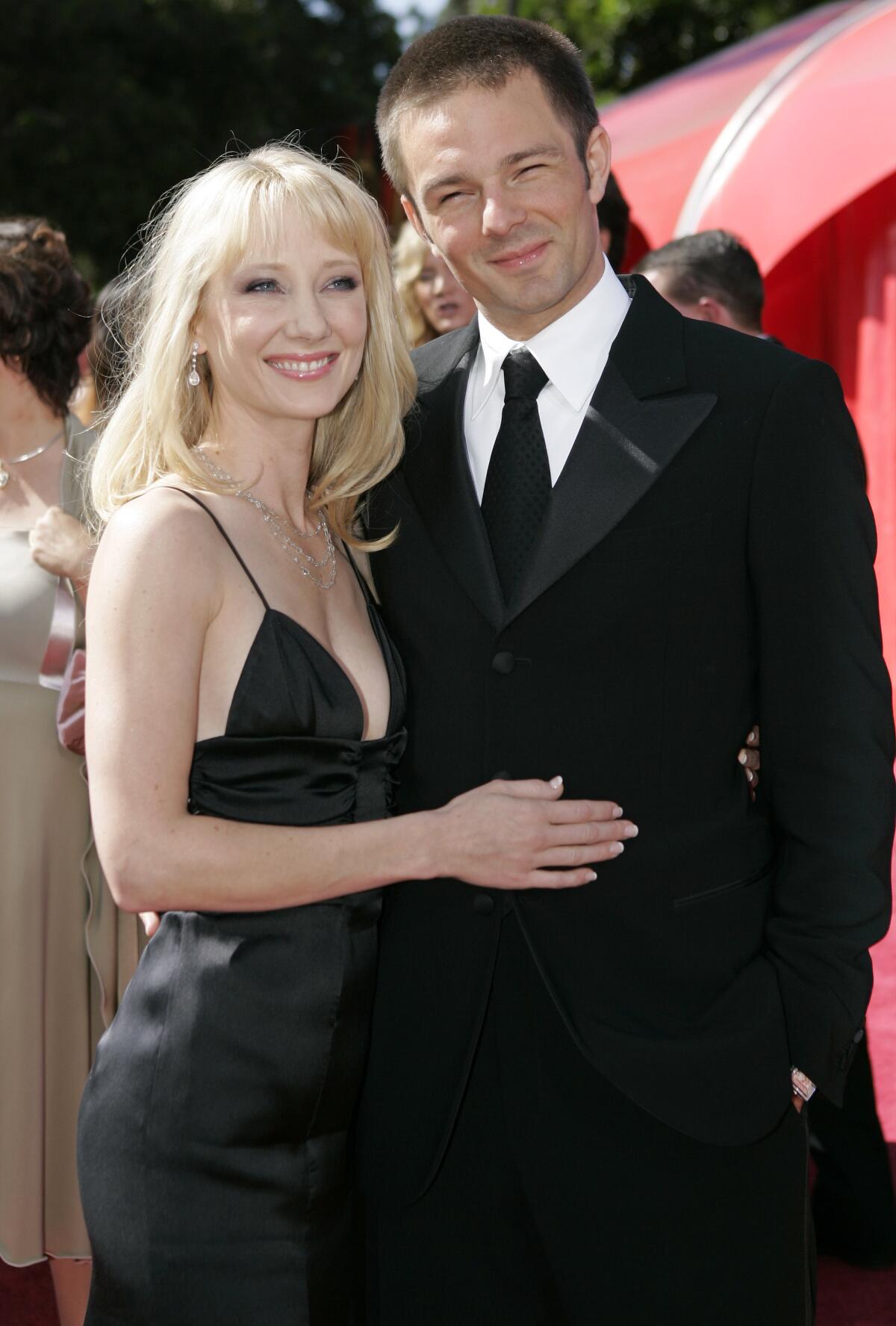 A blonde woman in a black dress embraces a man in a suit