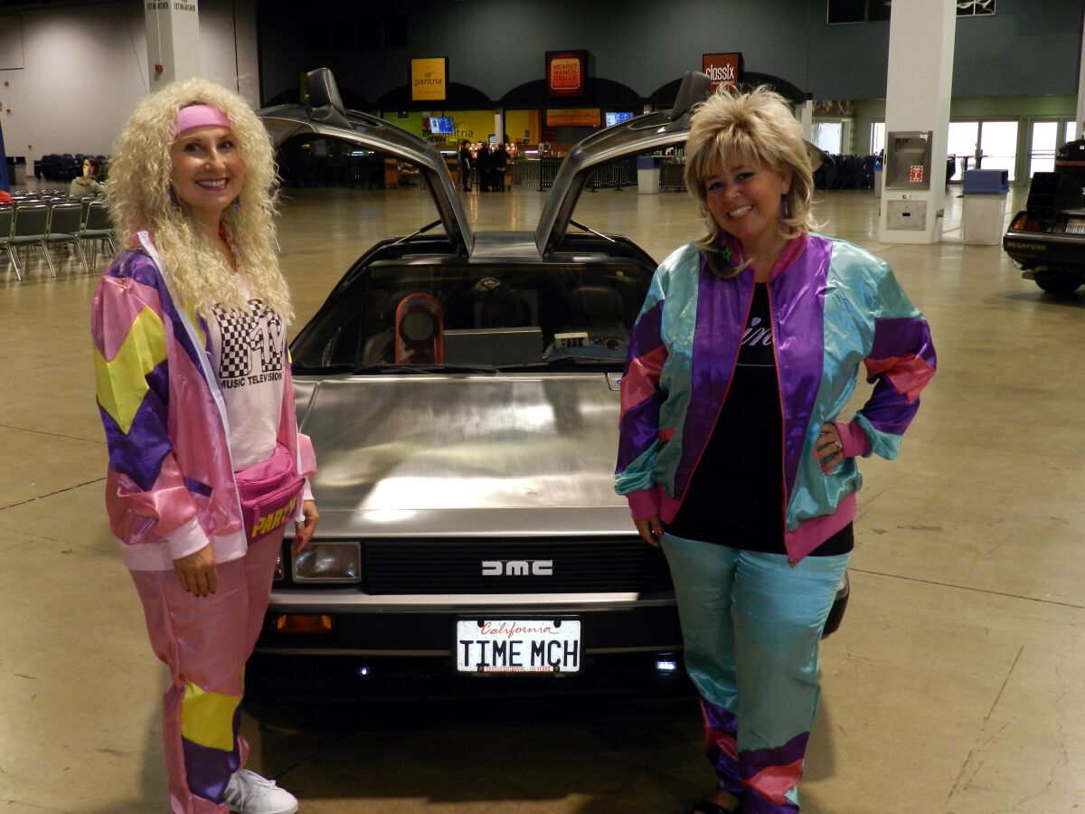 Cosplayers wearing clothes inspired by the movie "Back To The Future Part II" stand next to a DeLorean at NostalgiaCon 2019.