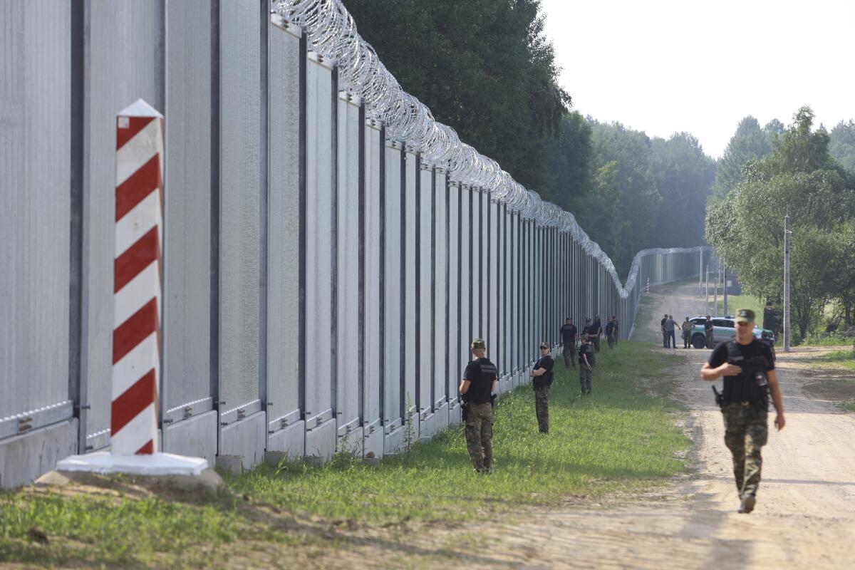 Border guards patrol along a tall metal wall.