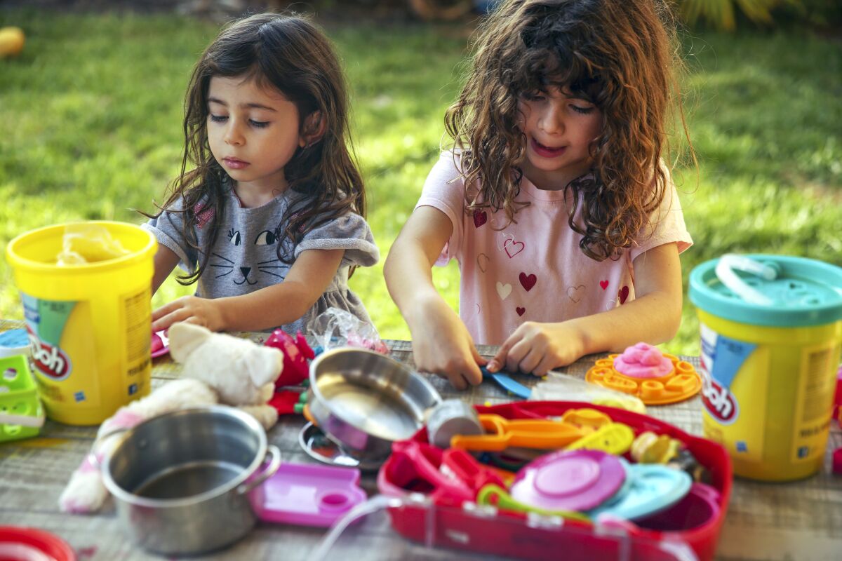 Scarlet and Lilah Knight make art with Play-Doh outdoors.