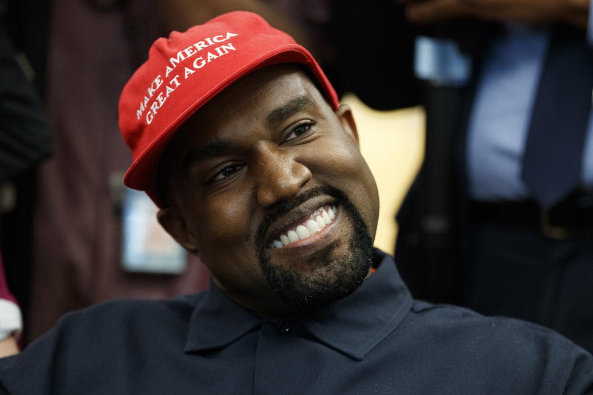 Kanye West wears a red hat with Trump's "Make America Great Again" slogan.