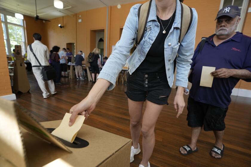 A man, right, waits as a woman drops her ballot into a box a polling place in Redfern as Australians cast their final votes in Sydney, Saturday, Oct. 14, 2023, in their first referendum in a generation that aims to tackle Indigenous disadvantage by enshrining in the constitution a new advocacy committee. The prospect of an Indigenous Voice to Parliament has bitterly divided Australia's Indigenous minority as well as the wider community. (AP Photo/Rick Rycroft)