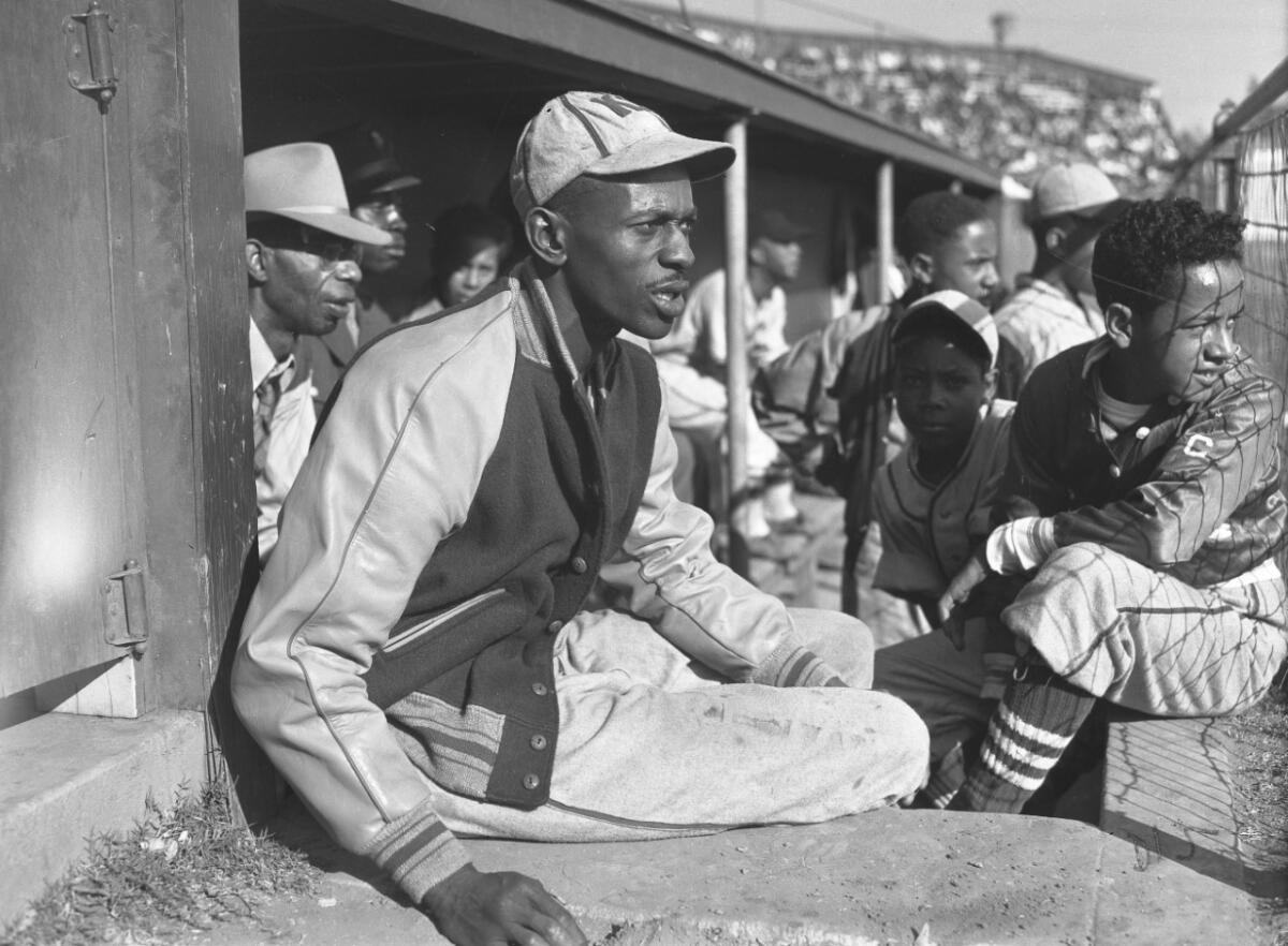 A man in a baseball cap and jacket appears riveted as he looks in a baseball dugout alongside several boys.