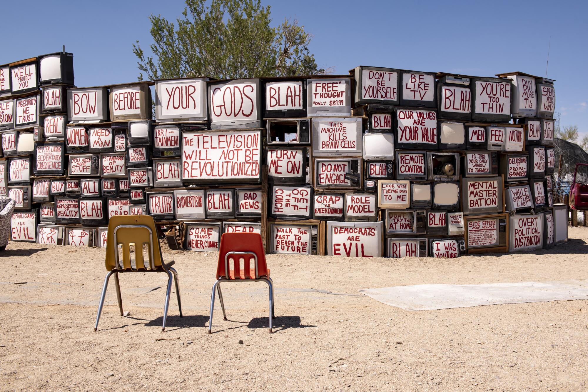 A wall of televisions, with white screens bearing messages in red letters, in an outdoor setting