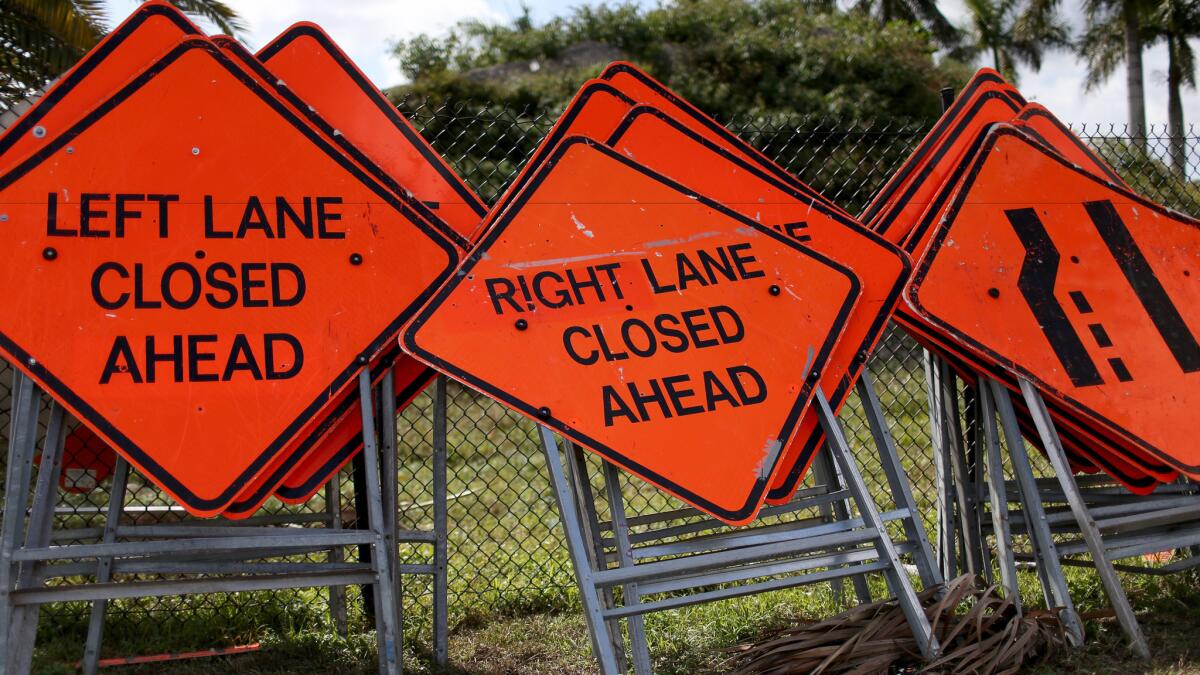 Construction work signs are stacked against a fence.