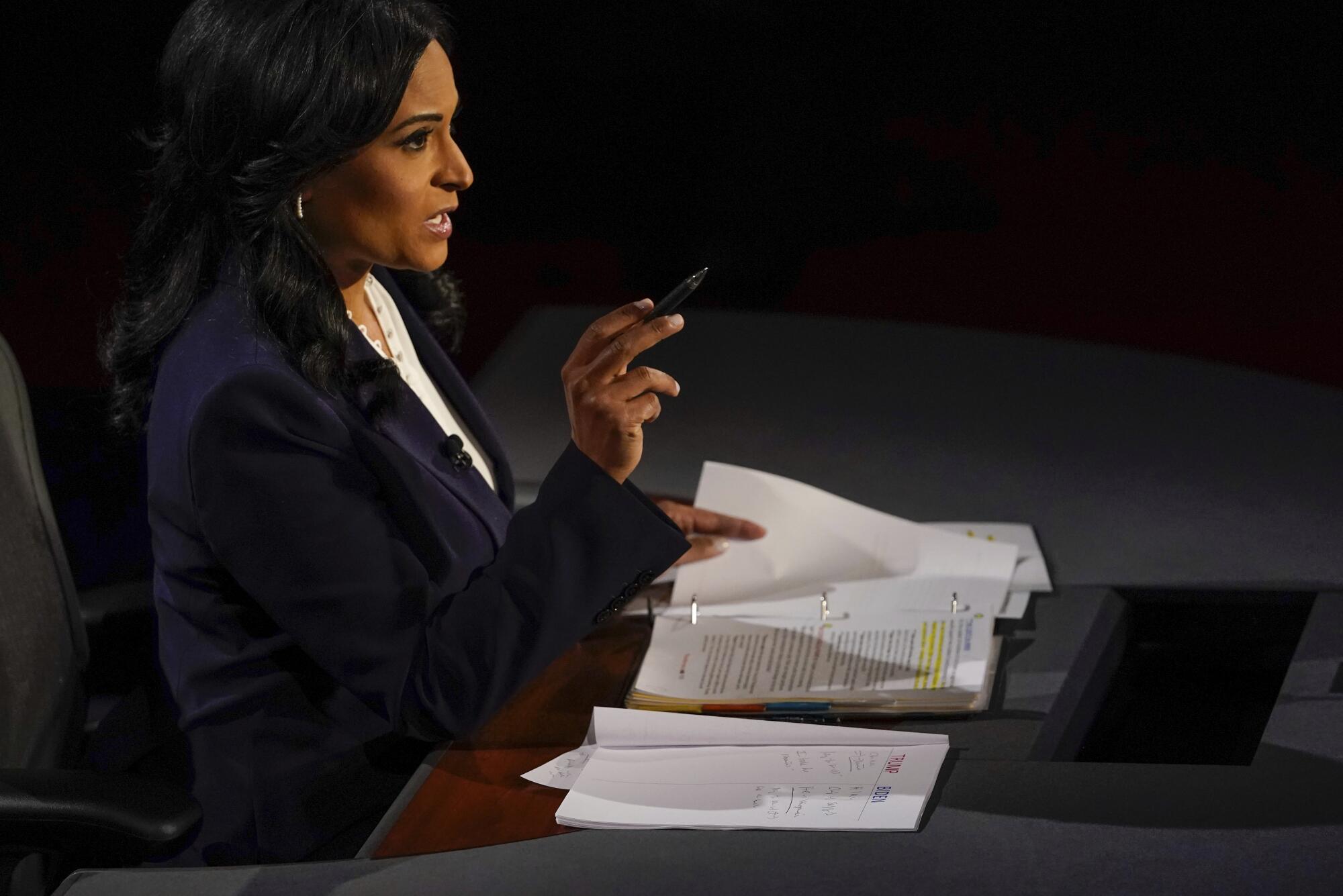 Moderator Kristen Welker gestures with a pen in her hand sitting in front of notes on her desk
