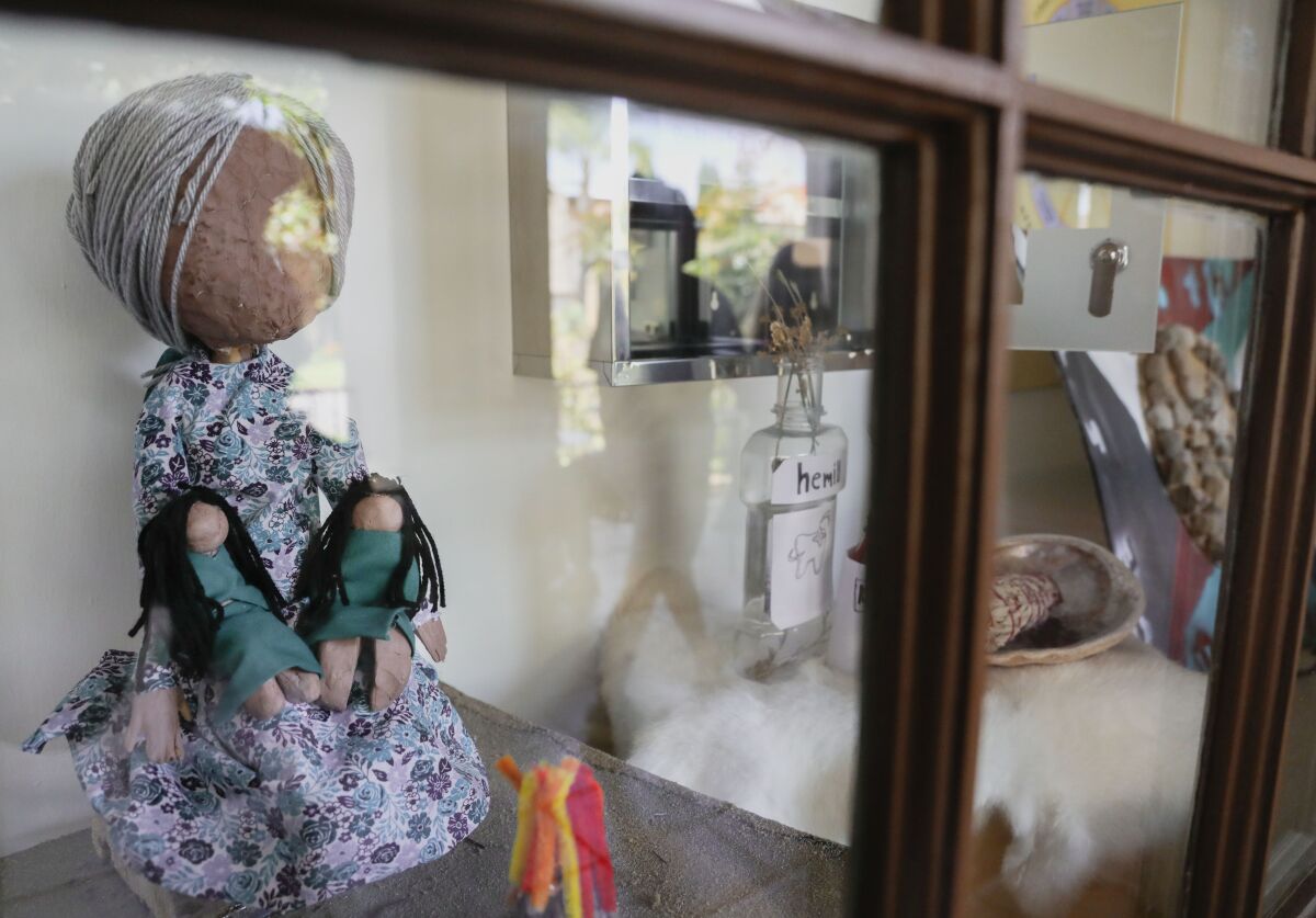 a large doll in a floral dress holding two small dolls wearing green dresses inside a glass display case