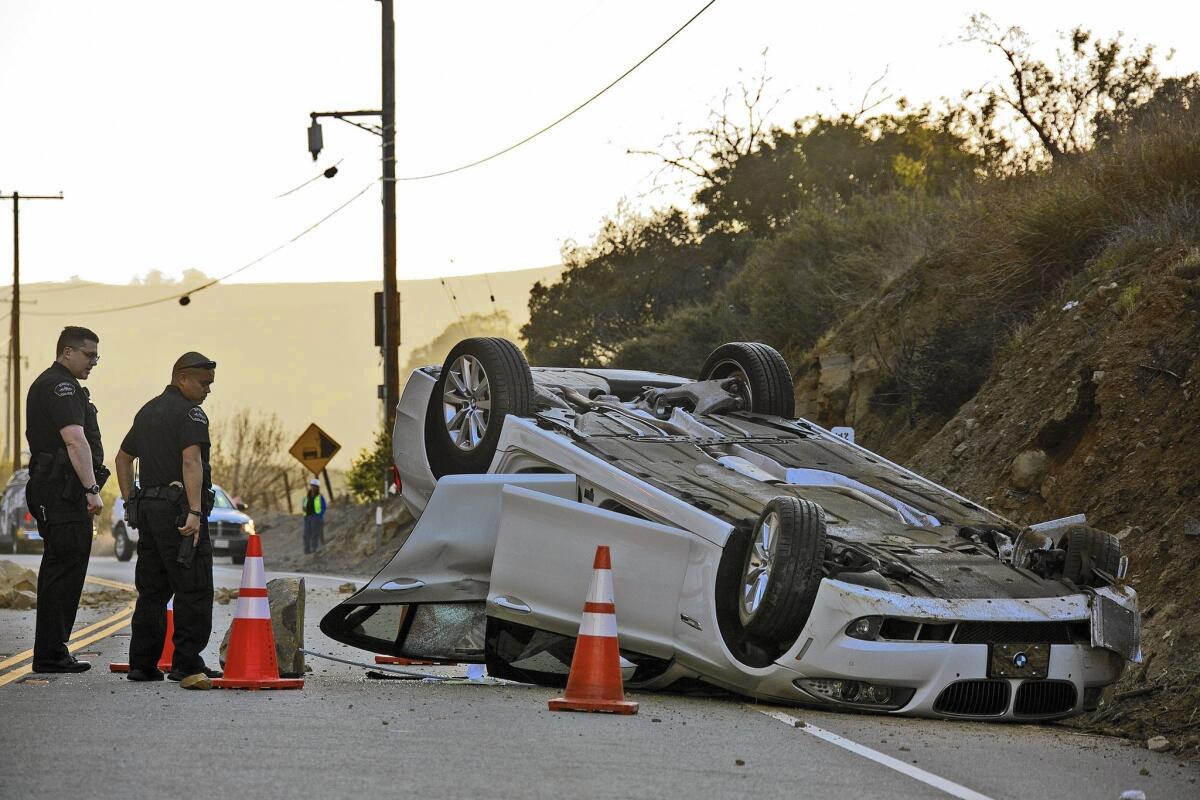 Caltrans workers and Brea police inspect a BMW that overturned during a rock slide in Carbon Canyon after the 5.1 La Habra earthquake last year.