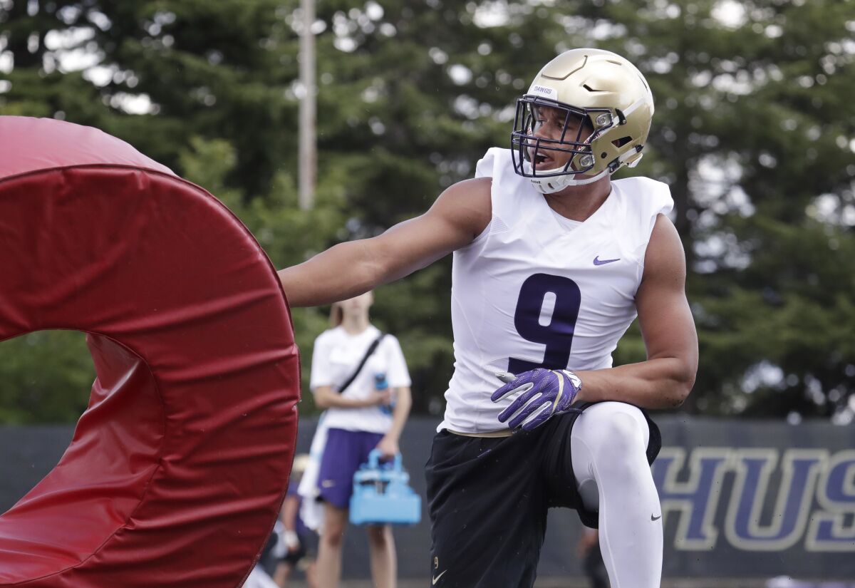 Washington's Joe Tryon kneels with a tackling dummy during practice.